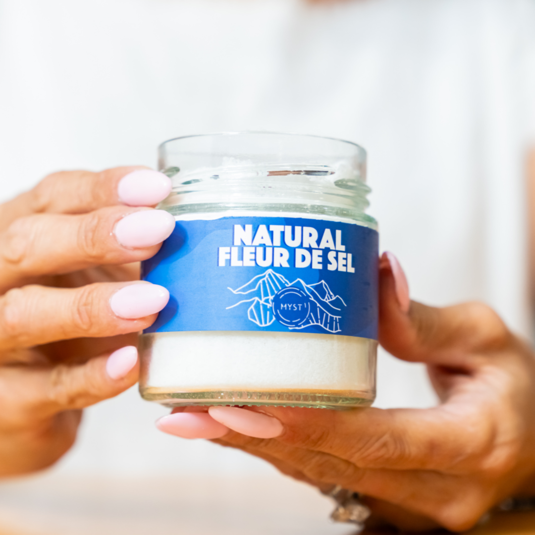 Person holding a jar of 'Natural Fleur de Sel' with a blue label.