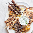 Platter of grilled skewers with naan bread and lemon wedges on a light background
