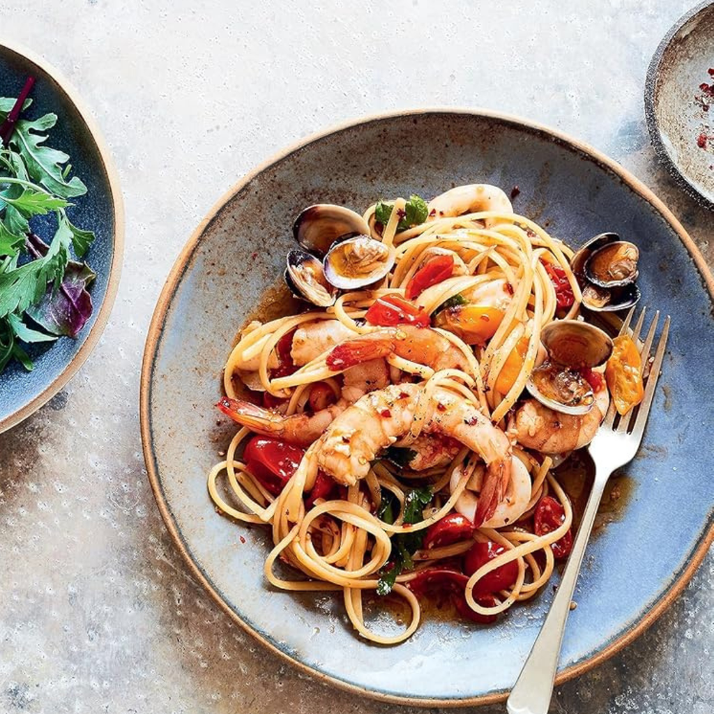 Plated dish of pasta with shrimp and clams on a textured surface
