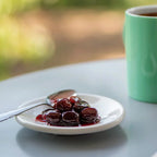 Plate of cherries with a spoon on a table next to a green mug.