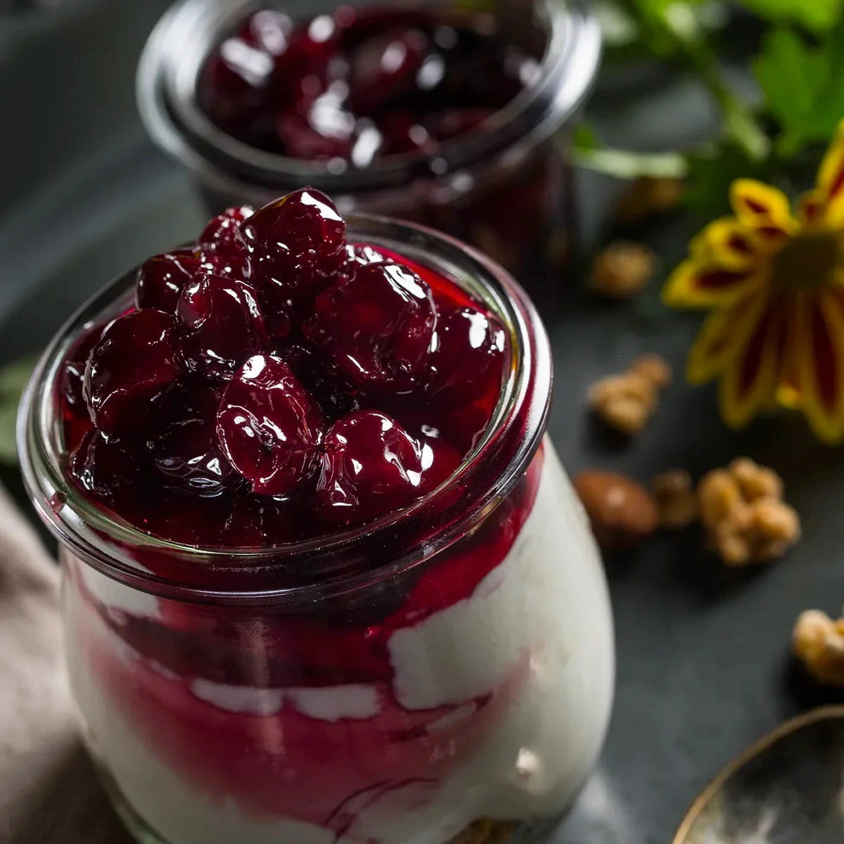 Glass jar filled with a layered dessert topped with red fruit compote on a dark surface.
