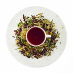 Tea cup with red liquid surrounded by dry herbs and leaves on a white plate