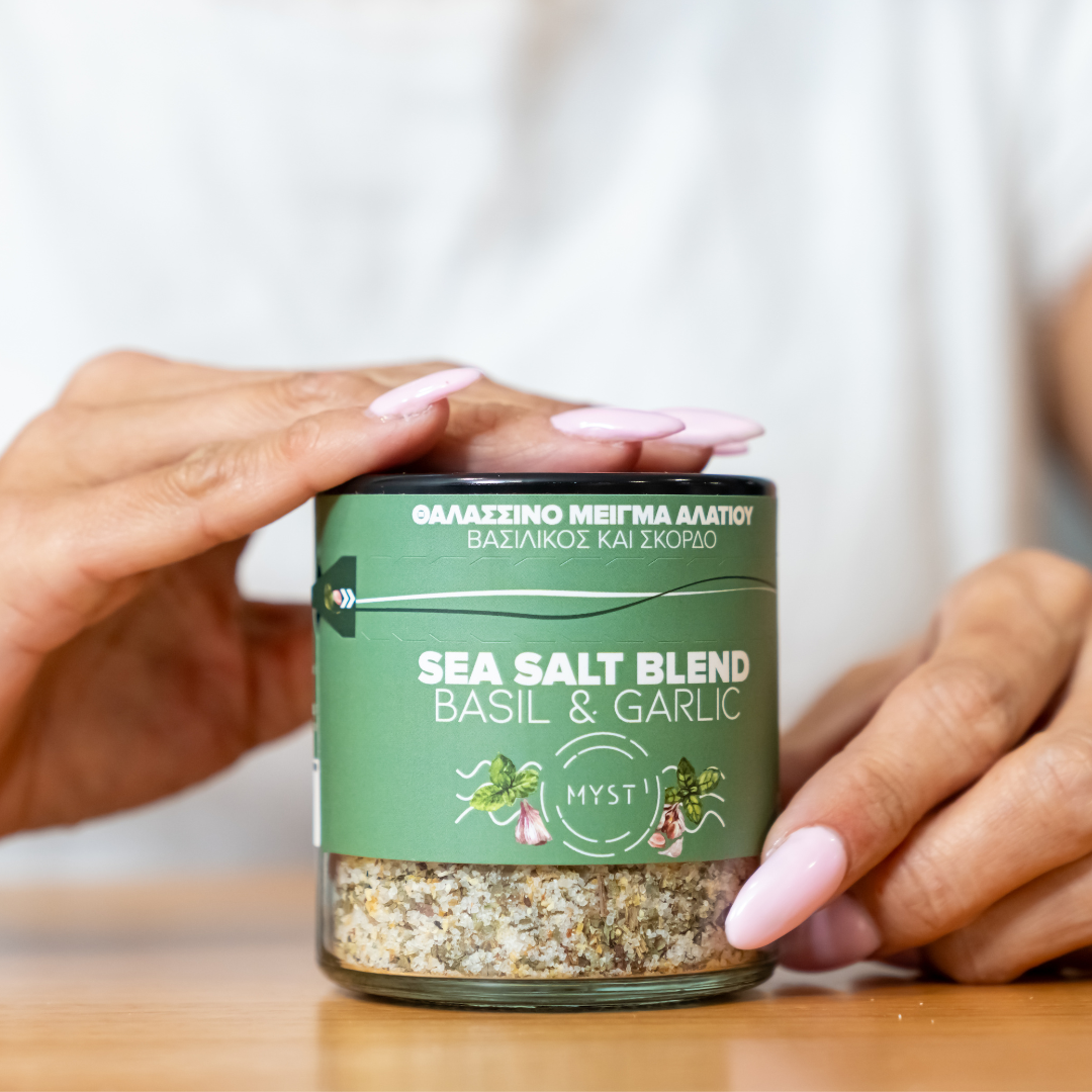 Person holding a jar of sea salt blend with basil and garlic on a wooden surface.