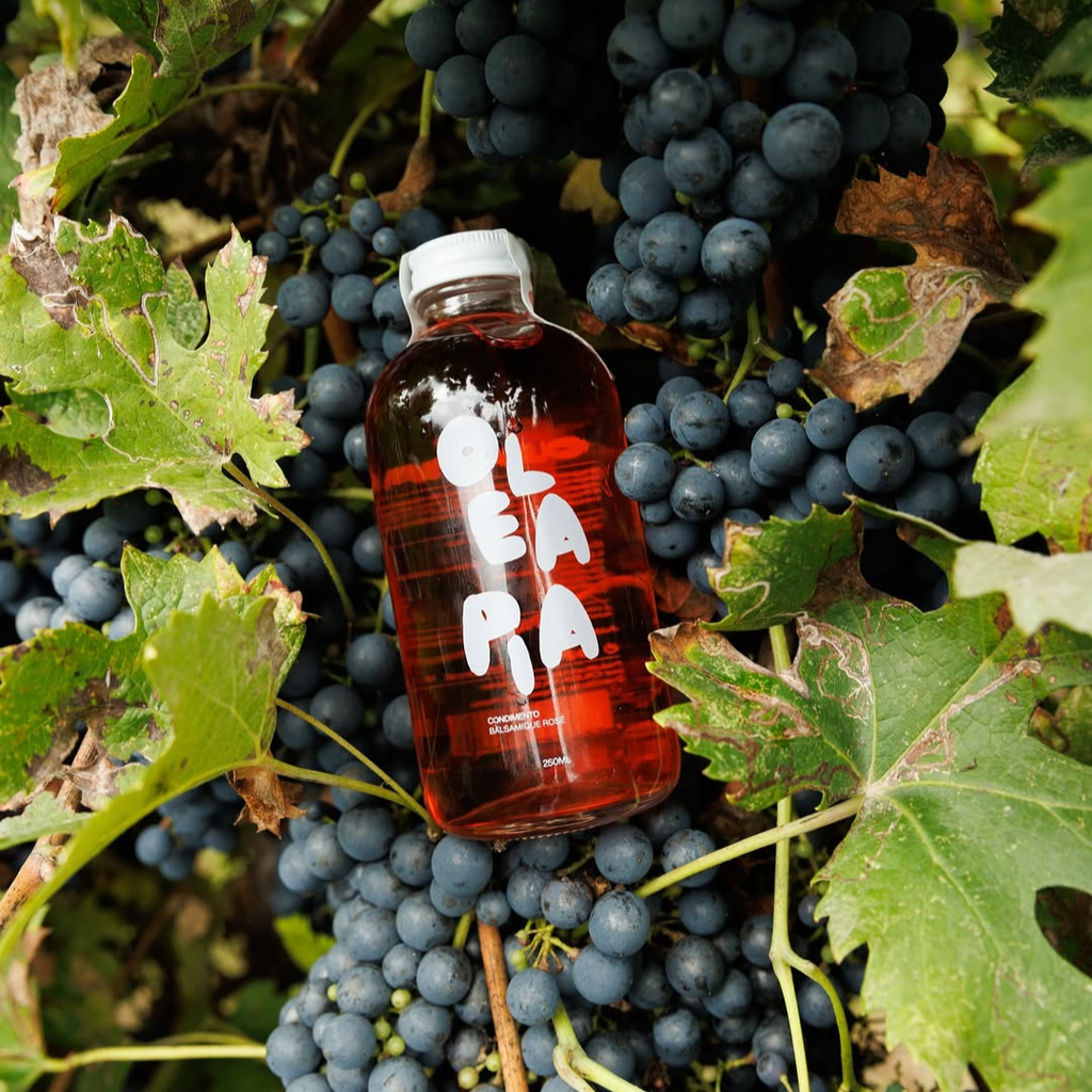 Bottle of red liquid with a white cap on a background of dark grapes and green leaves.