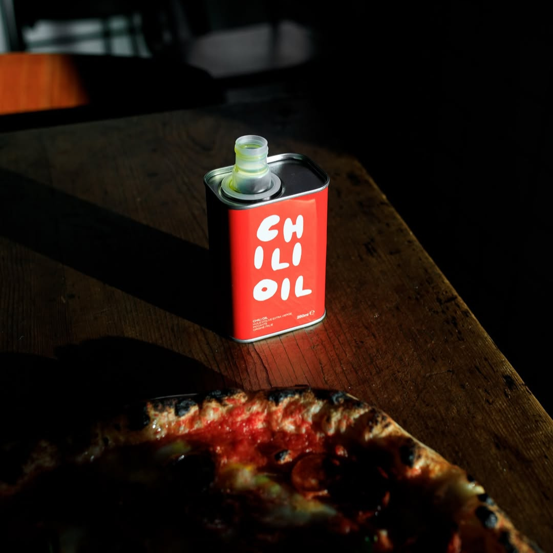Can of chili oil on a wooden table with a pizza in the foreground