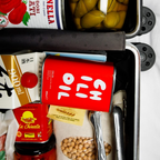 Open toolbox with various items including a can of olive oil, a bottle of La Chinata, and a box of Sapporo beer.
