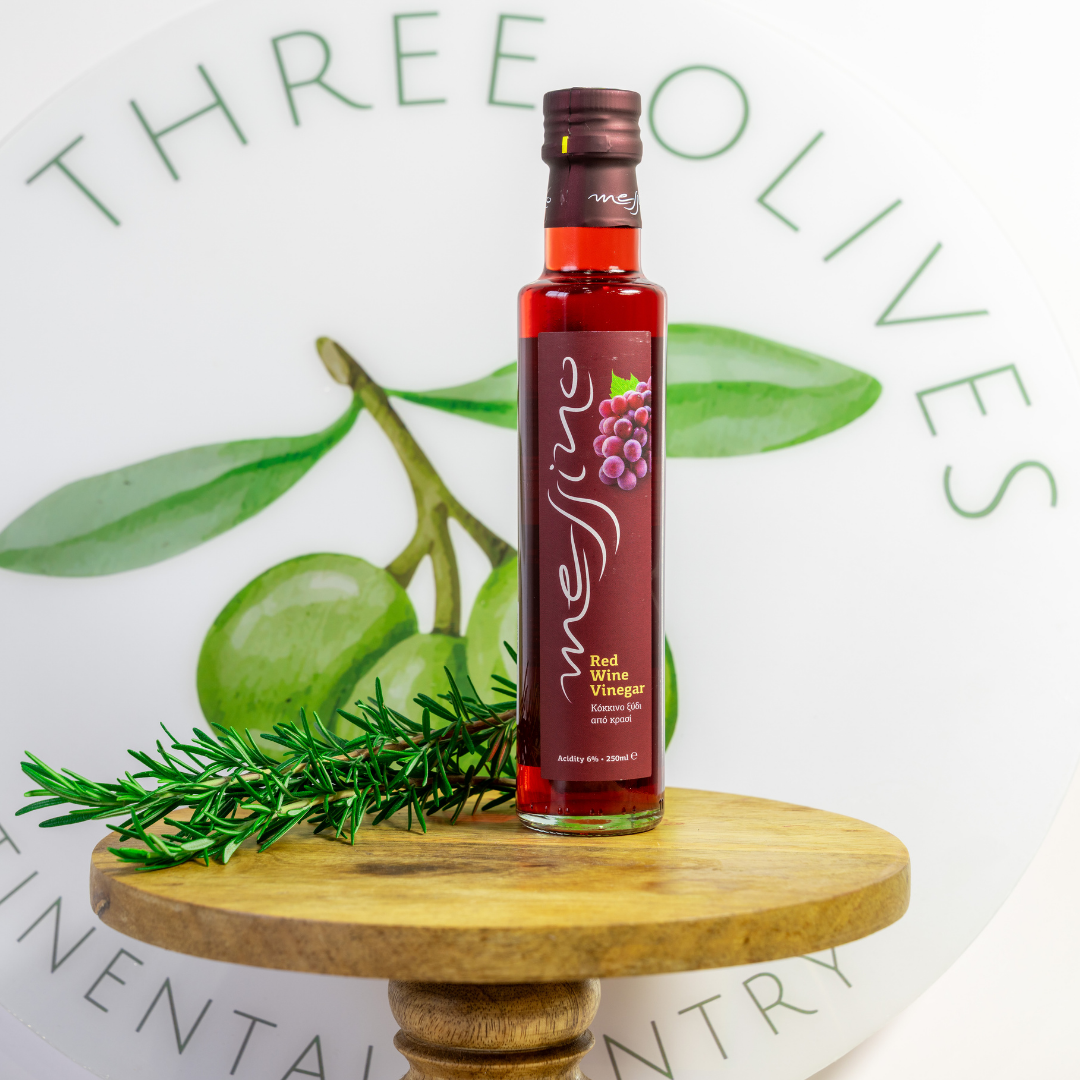 Bottle of Messina Red Wine Vinegar on a wooden stand with green olives and rosemary, branded 'Three Olives'.