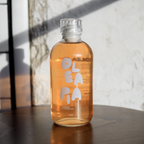 Bottle of OLA PA juice on a wooden surface with a light background
