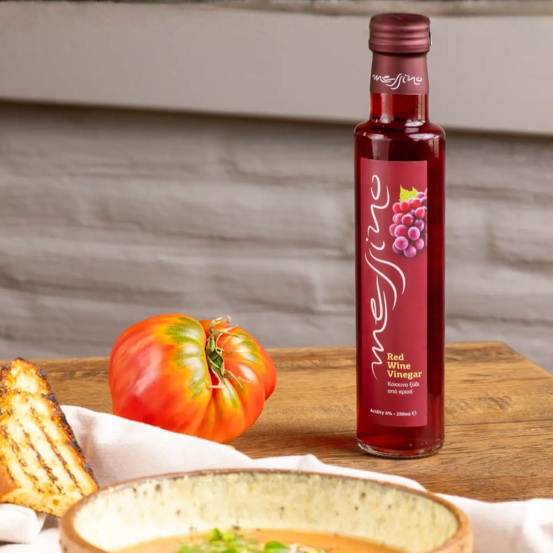 Bottle of red wine vinegar on a wooden surface with a tomato and bread in the background