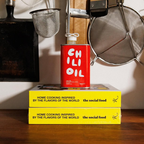 Red can of chili oil on top of two yellow cookbooks with a kitchen background