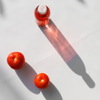 Red bottle and two tomatoes on a white surface with shadows