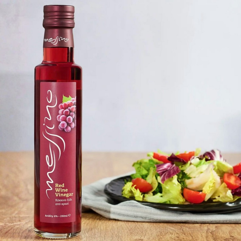 Bottle of red wine vinegar next to a salad on a wooden table
