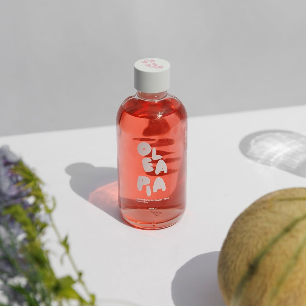 Bottle of Oleaia on a white surface with a melon and lavender in the background