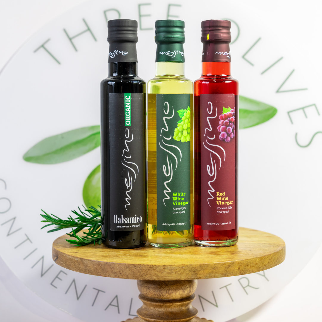 Three bottles of Messina Vinegars on a wooden stand with a white background featuring green leaves.